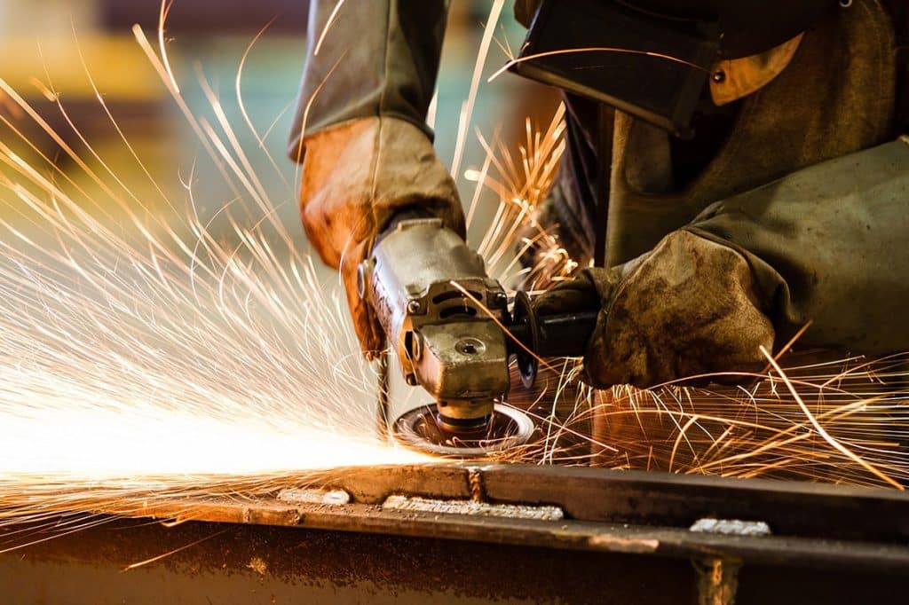 A close-up view of a steel worker working with a tool on a piece of metal throwing vibrant sparks as he works